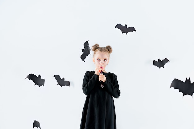 Bruja niña en vestido largo negro y accesorios mágicos.