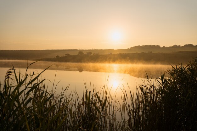 Brumoso verano lago amanecer. Salida del sol sobre el lago Superior en una brumosa mañana de verano