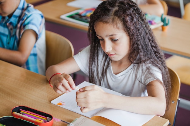 Brunette niña sentada en el escritorio de la escuela