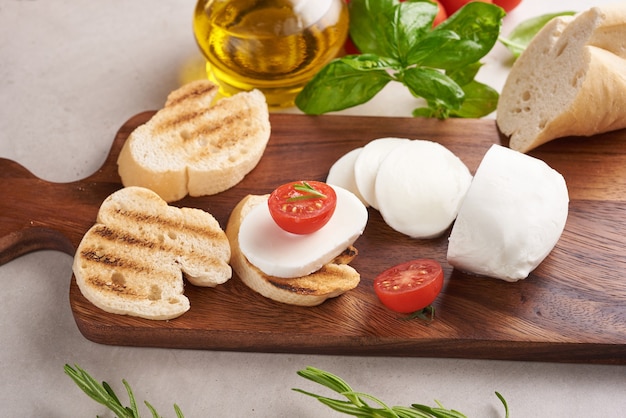 Bruschetta fresca con tomates, queso mozzarella y albahaca sobre una tabla para cortar. Aperitivo o refrigerio italiano tradicional, antipasto. Vista superior. Endecha plana. Chapata con tomate cherry.