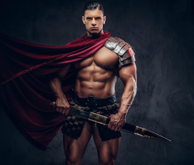 Brutal guerrero de la antigua Grecia con un cuerpo musculoso en uniformes de batalla posando sobre un fondo oscuro.