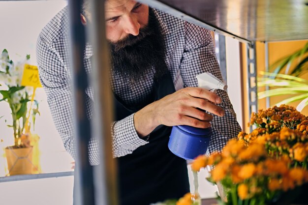 Brutal vendedor de flores barbudo con tatuajes en los brazos en una floristería.