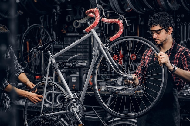 Buen trabajo en equipo de dos buenos hombres en un ajetreado taller de bicicletas. Los hombres llevan camisas a cuadros.