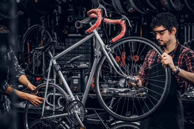 Buen trabajo en equipo de dos buenos hombres en un ajetreado taller de bicicletas. Los hombres llevan camisas a cuadros.