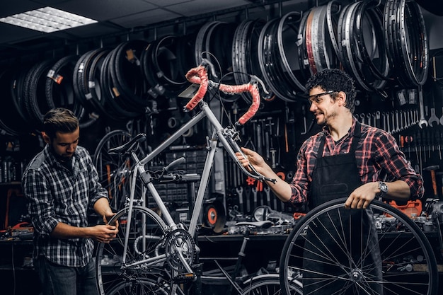 Foto gratuita buen trabajo en equipo de dos buenos hombres en un ajetreado taller de bicicletas. los hombres llevan camisas a cuadros.