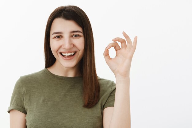 Buen trato, confírmalo. Morena europea optimista feliz y despreocupada en camiseta verde oliva que muestra el signo bien y sonriendo encantada como recomendando el producto, sin problemas con un servicio excelente