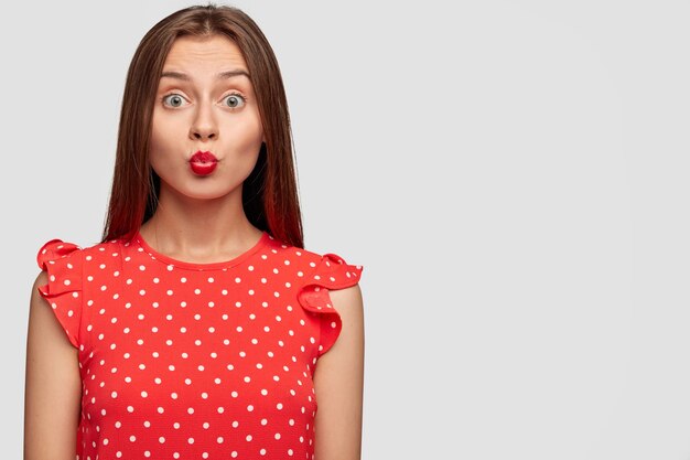 Buena mujer con lápiz labial rojo posando contra la pared blanca