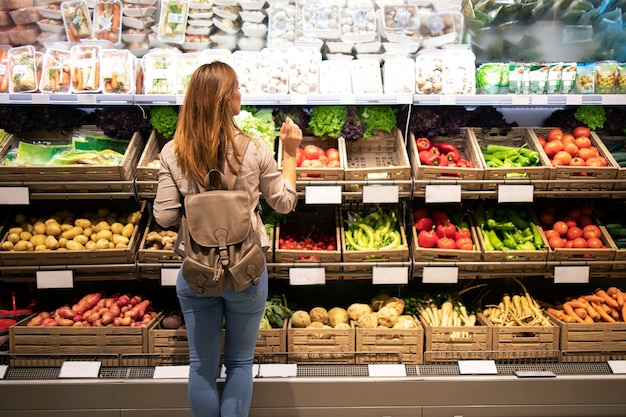 Buena mujer de pie delante de los estantes de verduras eligiendo qué comprar