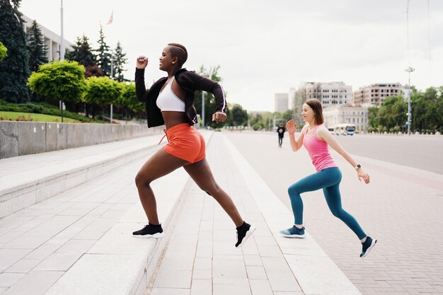 Buenos amigos en ropa deportiva corriendo en la ciudad hablando de mujeres multiétnicas haciendo ejercicio físico