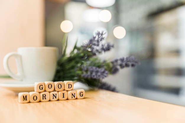 Buenos días bloques cúbicos con taza de café en el escritorio de madera