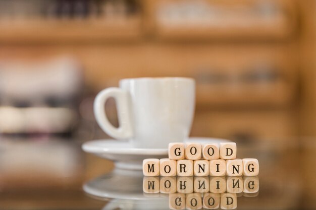 Buenos días bloques cúbicos y taza de café en el escritorio de vidrio reflexivo