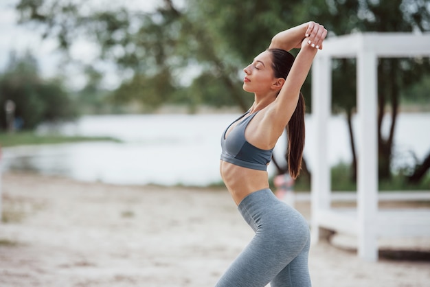 Buenos dias tiempo. Morena con forma de cuerpo agradable en ropa deportiva tiene día de fitness en la playa