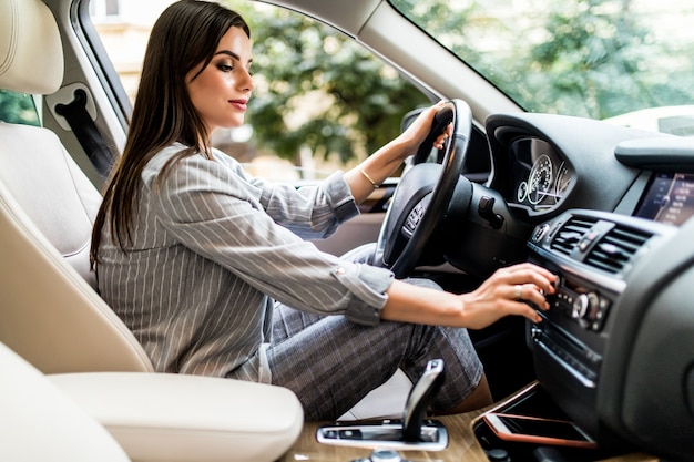 Buscando música favorita. Mujer atractiva joven sonriendo y presionando botones mientras conduce un coche