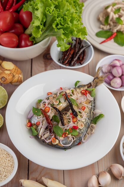 Caballa frita con galanga, pimienta, menta, cebolla roja en un plato blanco.