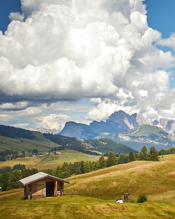 Foto gratuito una cabaña de madera en una tierra verde bajo nubes blancas con hermosas montañas