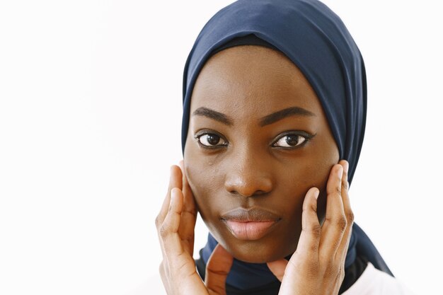 En la cabeza de la encantadora mujer musulmana religiosa satisfecha con una sonrisa suave, piel oscura y saludable, lleva un pañuelo en la cabeza. Aislado sobre fondo blanco.