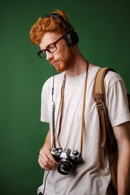 Cabeza lectora Yong hipster barbudo con mochila con cámara retro, escuchando música,