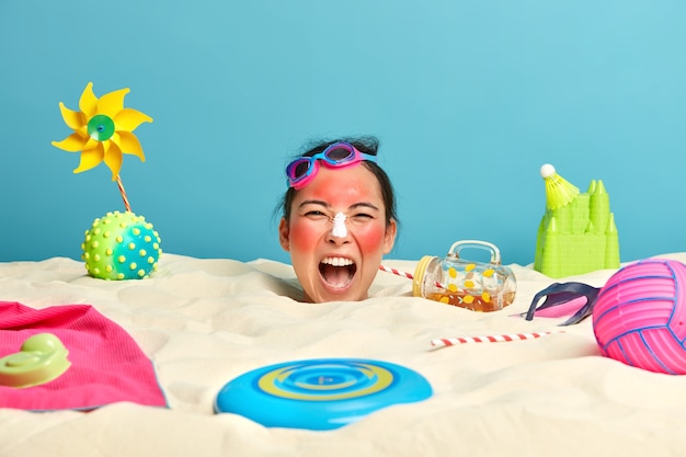 Cabeza de mujer joven con crema de protección solar en la cara rodeada de accesorios de playa