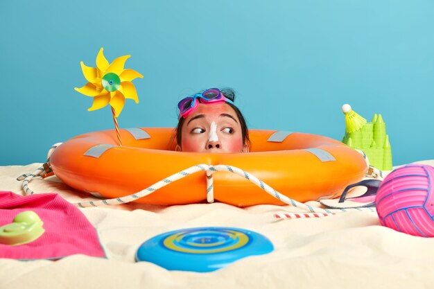 Cabeza de mujer joven con crema de protección solar en la cara rodeada de accesorios de playa