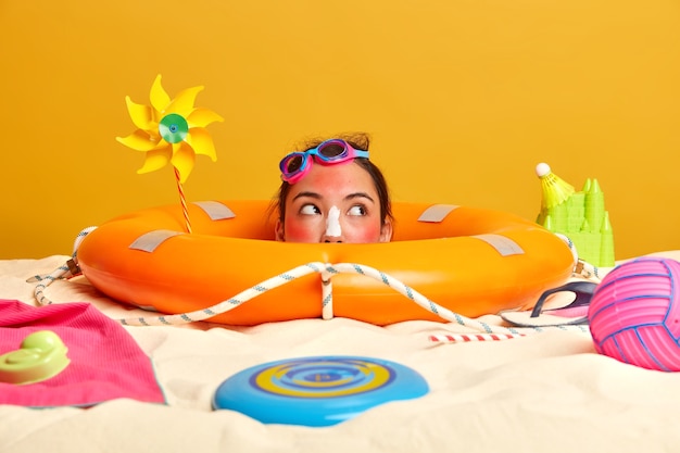 Cabeza de mujer joven con crema de protección solar en la cara rodeada de accesorios de playa