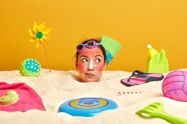 Cabeza de mujer joven con crema de protección solar en la cara rodeada de accesorios de playa