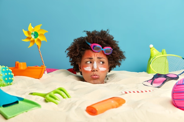 Cabeza de mujer joven con crema de protección solar en la cara rodeada de accesorios de playa