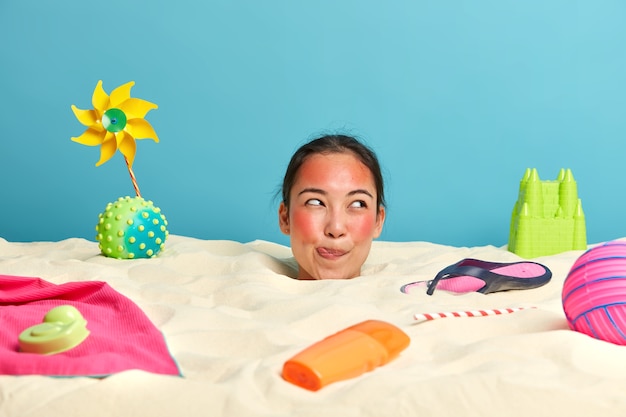 Cabeza de mujer joven con crema de protección solar en la cara rodeada de accesorios de playa