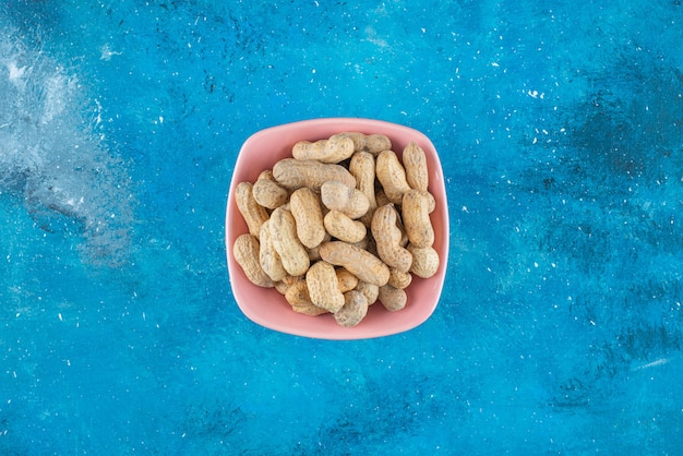 Cacahuetes con cáscara en un plato sobre la superficie azul