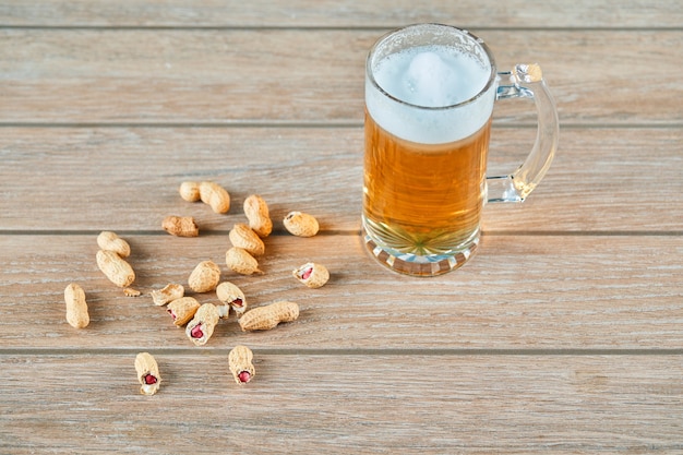 Foto gratuita cacahuetes y un vaso de cerveza en la mesa de madera.