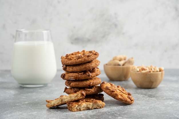 Cacahuetes, vaso de leche y galletas con cacahuetes orgánicos sobre mesa de mármol.