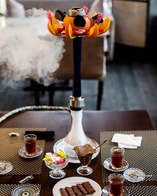 Cachimba decorada con naranja y flores y té con dulces sobre la mesa