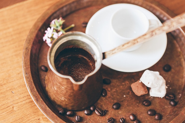 Café en un café café cobre y una taza de cerámica blanca en una bandeja con granos de café.