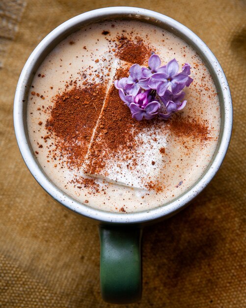 Café capuchino caliente con pétalos de flores en una taza sobre un saco