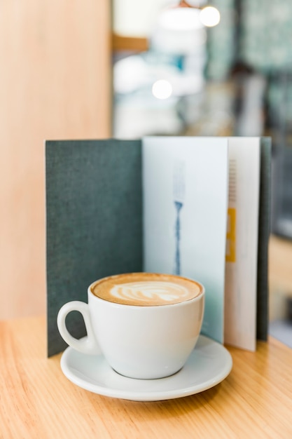 Café capuchino con latte de arte y menú en la mesa de madera