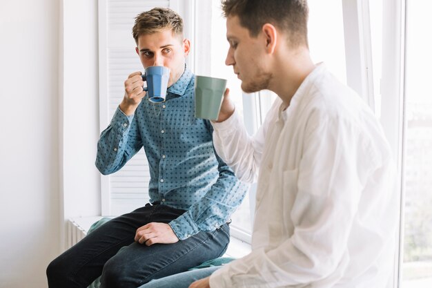 Café de consumición del hombre joven que se sienta cerca de ventana