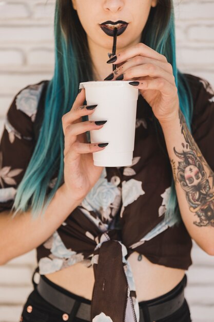 Café de consumición moderno de la mujer joven con la paja