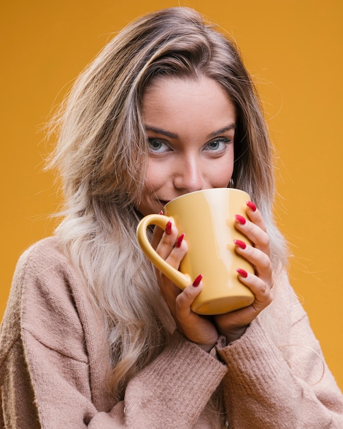 Café de consumición de la mujer joven contra fondo amarillo