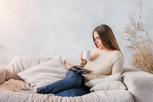 Foto gratuita café de consumición de la mujer joven mientras que lee el libro