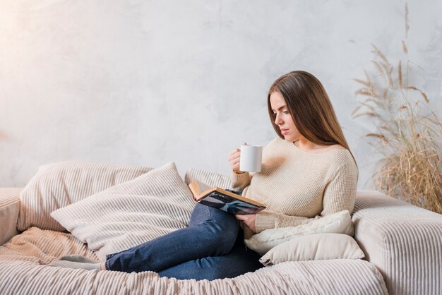 Café de consumición de la mujer joven mientras que lee el libro