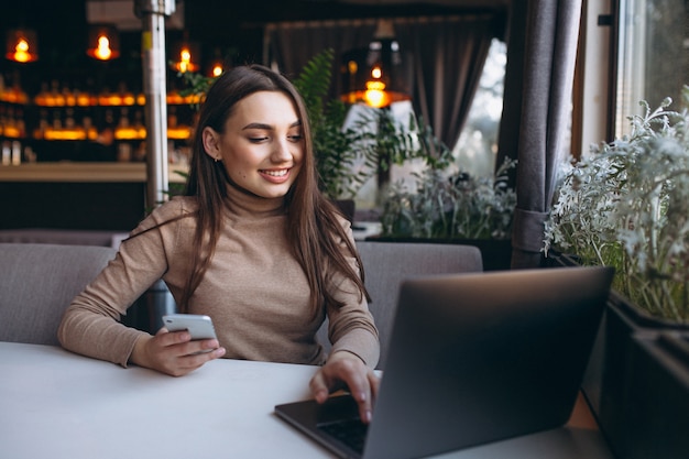 Café de consumición de la mujer de negocios y trabajo en la computadora portátil en un café