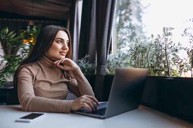 Café de consumición de la mujer de negocios y trabajo en la computadora portátil en un café