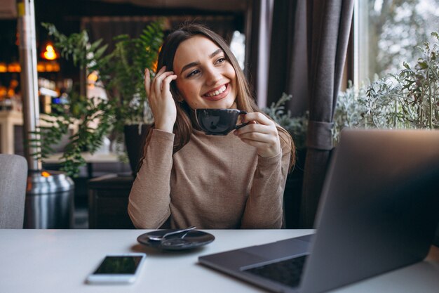 Café de consumición de la mujer de negocios y trabajo en la computadora portátil en un café