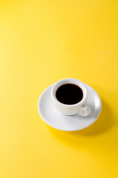 Café espresso en pequeña taza de cerámica blanca sobre fondo vibrante de color amarillo