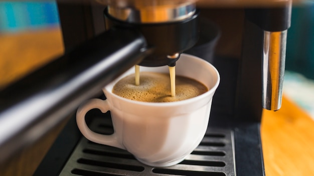 Café con espuma vertiendo desde la máquina de café espresso