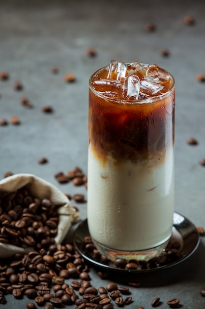 Café helado en un vaso alto con crema cubierto con café helado decorado con granos de café.