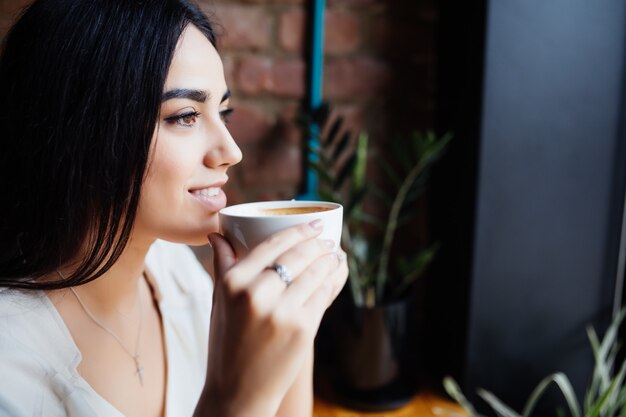 Café. Hermosa chica bebiendo té o café en la cafetería. Mujer modelo de belleza con la taza de bebida caliente. Tonos de colores cálidos