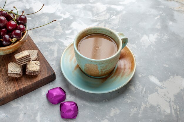 café con leche con caramelos, gofres y guindas en un escritorio gris claro