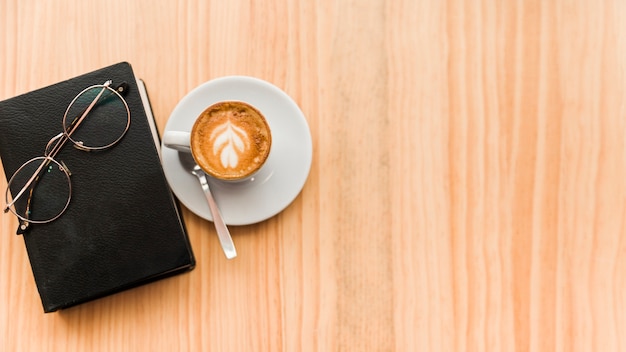 Café con leche con gafas y libro sobre fondo de madera