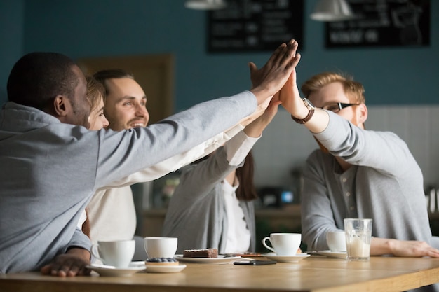 Foto gratuita café multirracial feliz de los amigos que da alto-cinco en la reunión en café