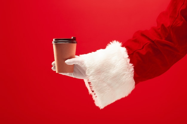 Café navideño. La mano de Santa sosteniendo una taza de café aislada en un rojo